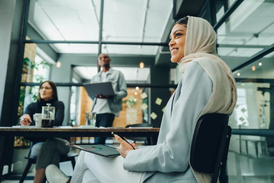 A photo of a smiling woman wearing a headscarf in a modern office.