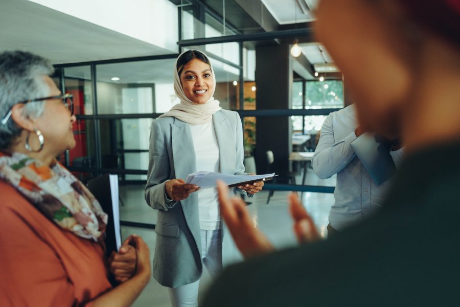 A photo of a young woman in a modern office wearing a head scarf among her colleagues